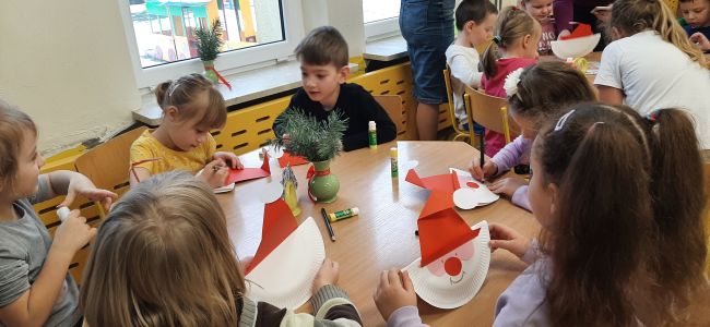 Dzieci siedzą przy stolikach i  wykonują pracę plastyczną