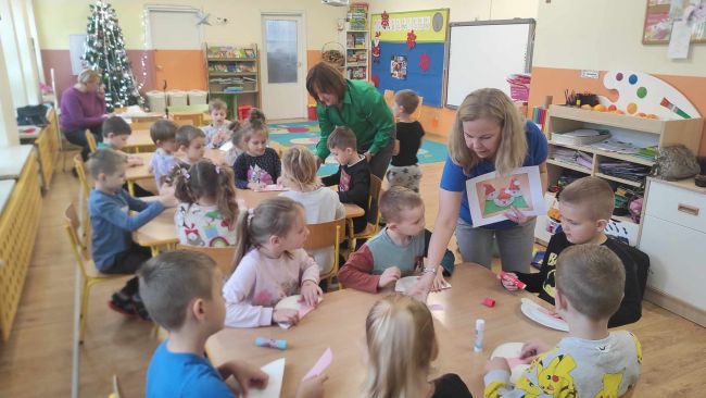 Dzieci siedzą przy stolikach i  wykonują pracę plastyczną