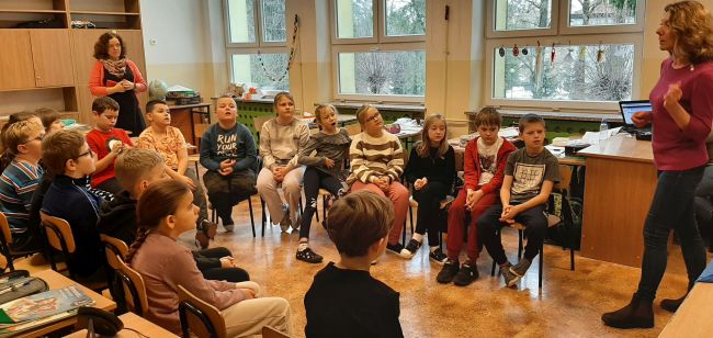 Klasa szkolna. Uczniowie siedzą na krzesłach w półokręgu. Prowadząca prezentuje teatrzyk Kamishibai.