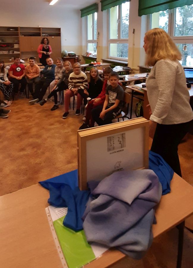 Biblioteka szkolna. Uczniowie siedzą na dywanie w półokręgu. Prowadząca prezentuje teatrzyk Kamishibai.
