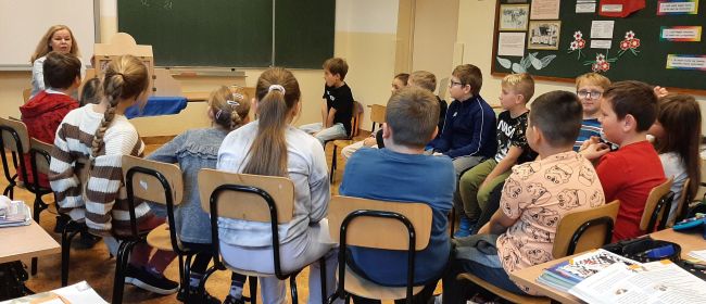 Klasa szkolna. Uczniowie siedzą na krzesłach w półokręgu. Prowadząca prezentuje teatrzyk Kamishibai.