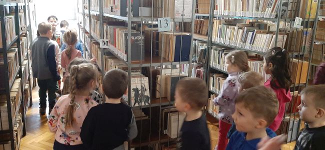 Dzieci zwiedzają bibliotekę. Buszują po półkach.