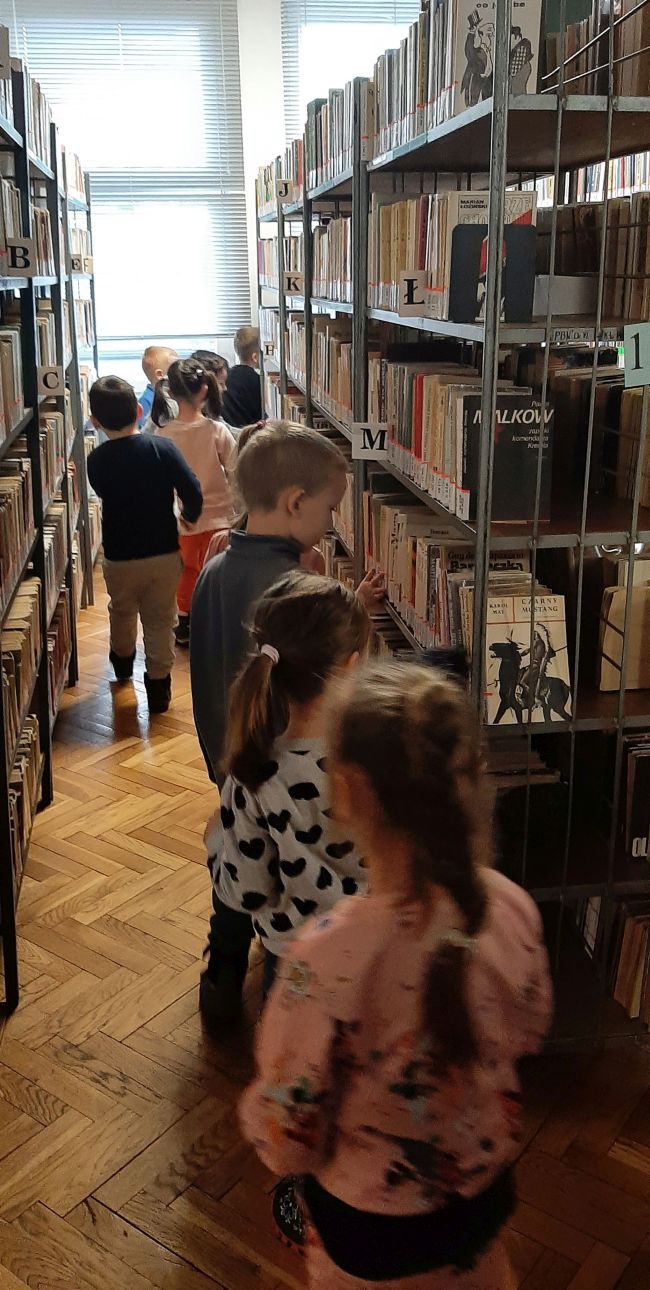 Dzieci zwiedzają bibliotekę. Buszują po półkach.