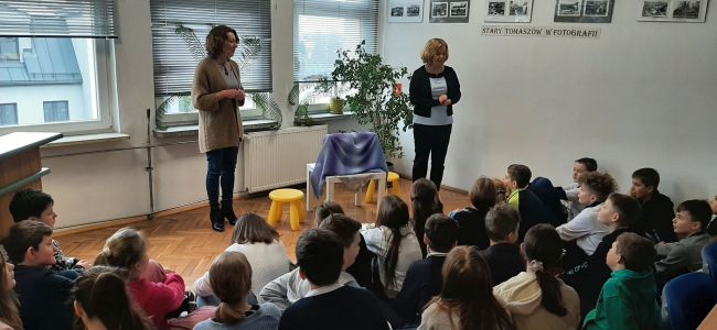 Prowadzące opowiadają bajkę ”Idzie wiosna, Wielkanoc tuż, tuż…” za pomocą teatrzyku Kamishibai. Uczniowie siedzą na podłodze i słuchają