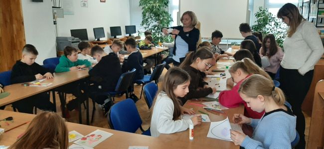 Uczniowie siedzą przy stolikach, wykonują prace plastyczną. Kolorują i dekorują papierowe jajka.