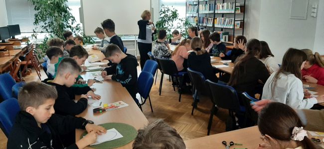 Uczniowie siedzą przy stolikach, wykonują prace plastyczną. Kolorują i dekorują papierowe jajka.