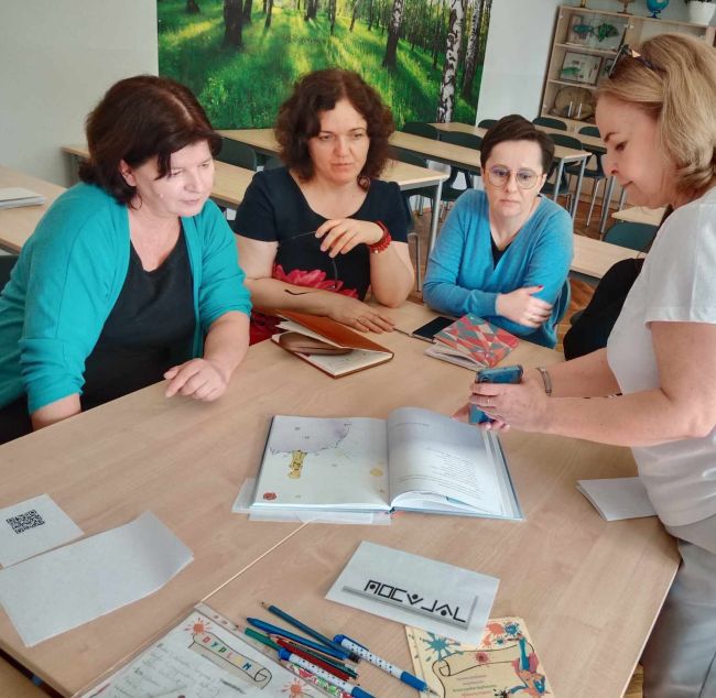 Nauczyciele oglądają książki z aplikacją do rozszerzonej rzeczywistości. Prowadząca pokazuje obrazy na telefonie