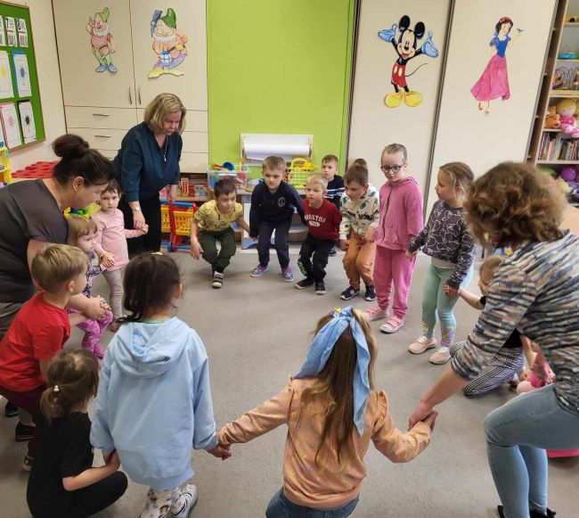 Przedszkolaki z opiekunami i prowadzącymi w trakcie zabawy ruchowej