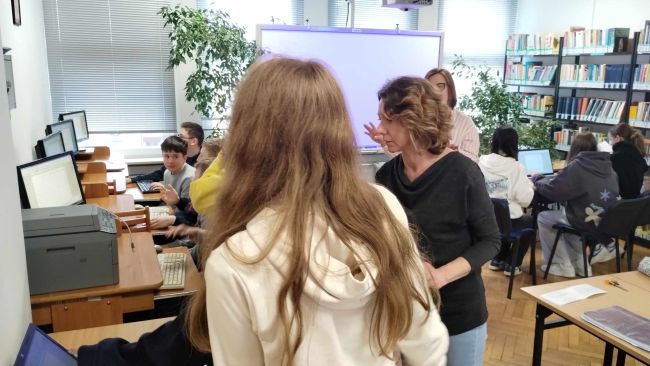 Czytelnia biblioteki. Uczniowie podzieleni na grupy siedzą przy komputerach redagując tekst zaproszenia.