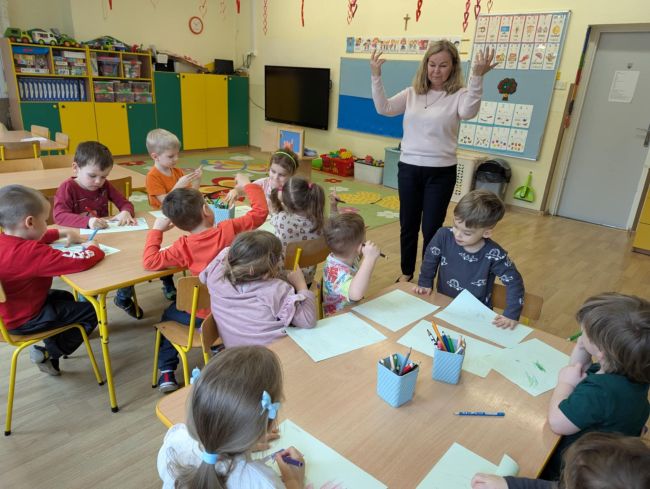 Dzieci siedzą przy stolikach i rysują
