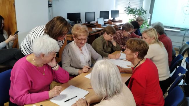 Nauczyciel prowadzi gimnastykę z koordynacji, a seniorzy stoją w kole i powtarzają.