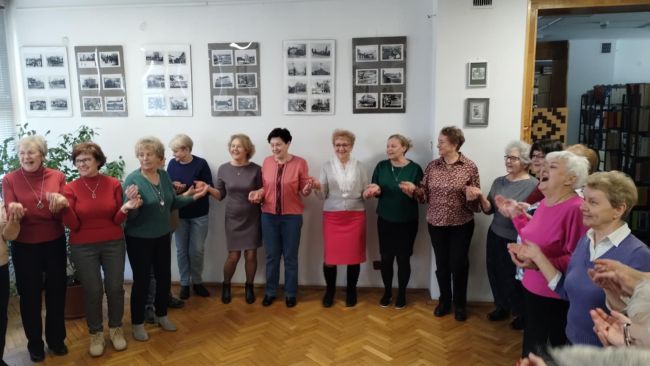 Seniorzy uczestniczą w zabawie „wyścig kubeczków” dmuchając przez słomki.