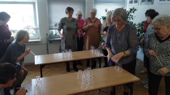 Uczestnicy warsztatów siedzą przy stolikach i wykonują gimnastykę rysunkową.