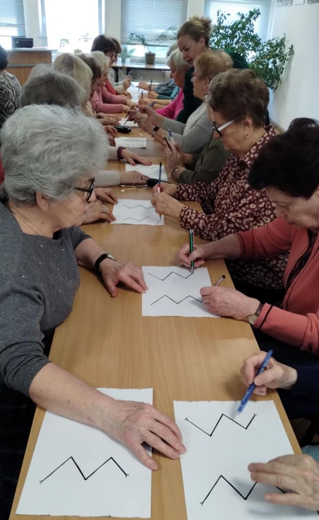 Uczestnicy warsztatów siedzą przy stolikach i wykonują  neuroćwiczenia wspierające pracę mózgu.
