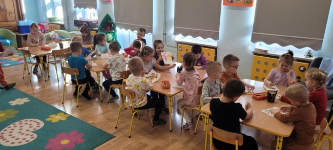 Dzieci siedzą przy stolikach i malują prace plastyczne.