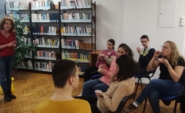 Nauczyciel stoi, prowadzi zajęcia, uczniowie siedzą i słuchają.