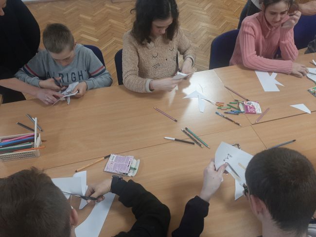 Uczniowie siedzą przy stołach i wykonują pracę plastyczną.