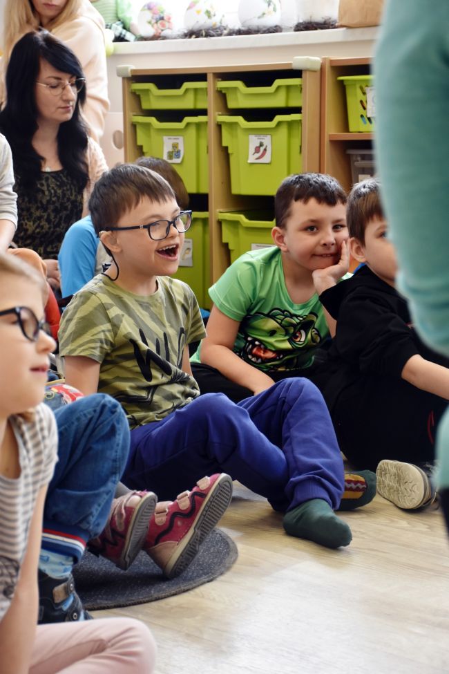 Dzieci siedzą na podłodze, słuchają opowieści.