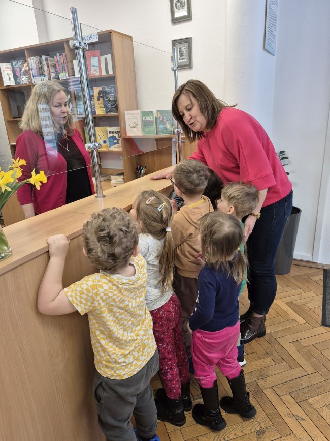 Nauczyciele rozmawiają z dziećmi, które stoją przy ladzie i słuchają.