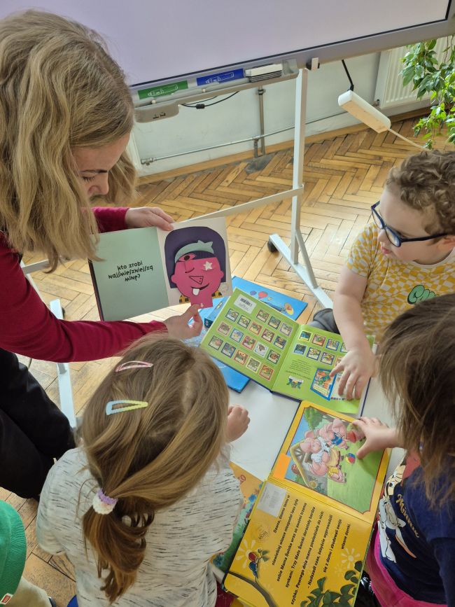 Nauczyciel pokazuje kreatywne książki, dzieci siedzą i oglądają.