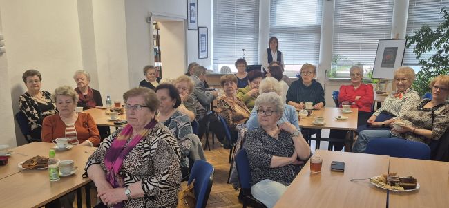 Spotkanie w czytelni Biblioteki Pedagogicznej. Uczestnicy siedzą przy stolikach, autorzy wystawy i prowadząca w centrum siedzą na fotelach, prowadzą rozmowę.