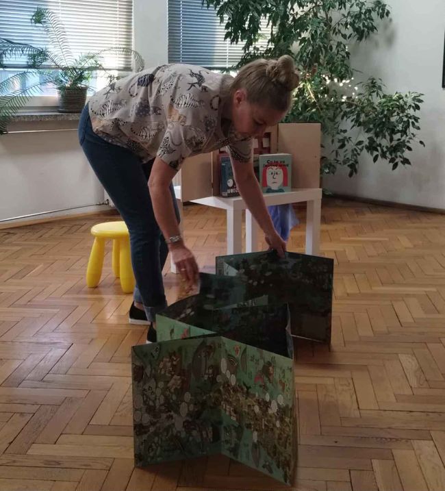 Prowadząca prezentuje kreatywną książkę. Rozkłada ją na podłodze.