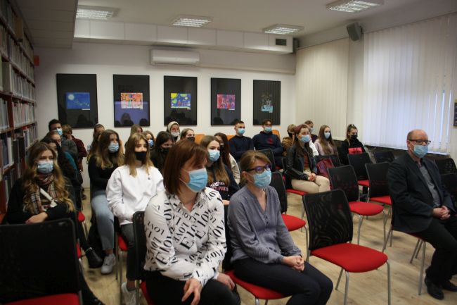 Na zdjęciu widoczna jest publiczność w czytelni biblioteki pedagogicznej, pracownicy biblioteki, nauczyciel oraz uczniowie z liceum.
