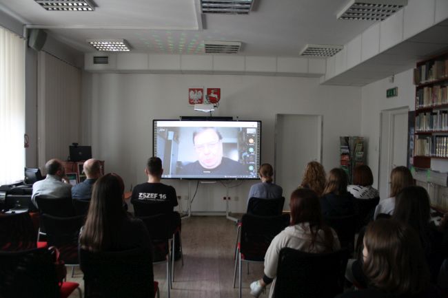 Na zdjęciu widoczna tablica interaktywna, a na niej prelegent Paweł Majka, który łączył się z Krakowa z uczestnikami. Na zdjęciu widoczni również uczestnicy konferencji przysłuchujący się prelekcji