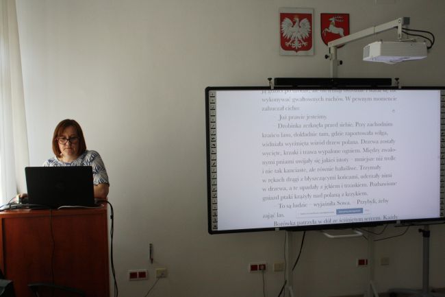 Nauczyciel bibliotekarz Biblioteki Pedagogicznej w Zamościu w tle tablica multimedialna z wyświetloną stroną opowiadania