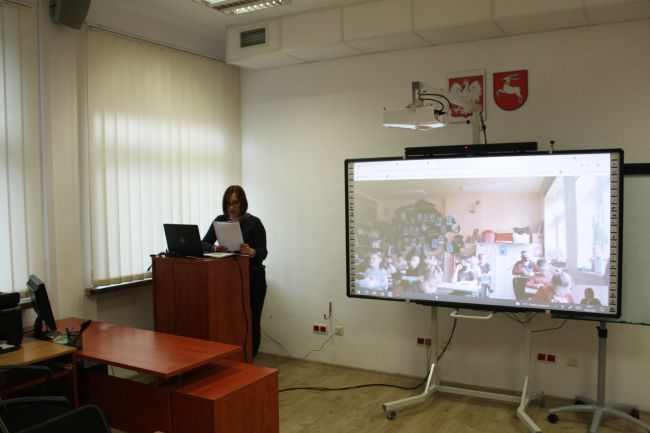  Nauczyciel bibliotekarz Biblioteki Pedagogicznej w Zamościu w tle tablica multimedialna z wyświetloną klasą - uczestnikami warsztatów online
