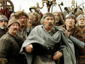 Kadr z filmu "Stara baśń. Kiedy słońce było bogiem" w reżyserii Jerzego Hoffmana. Na zdjęciu widać od frontu zgromadzenie mężczyzn w dawnych strojach, niektórzy mają na głowach dawne hełmy. Mężczyźni patrzą w jednym kierunku, wyglądają na poruszonych, zdziwionych, może nawet przerażonych.