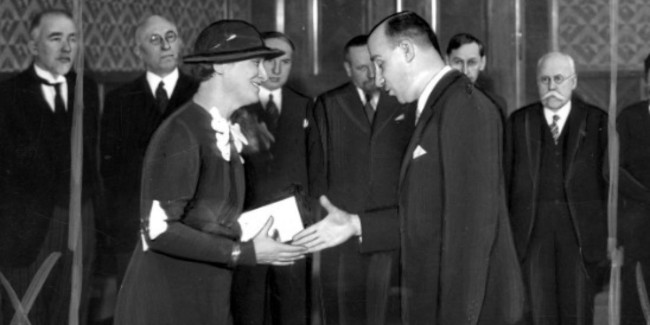 Czarno-białe zdjęcie przedstawia wręczenie Kazimierze Iłłakowiczównie Państwowej Nagrody Literackiej za rok 1934 przez ministra wyznań religijnych i oświecenia publicznego Wacława Jędrzejewicza w styczniu 1935. W tle widać różne zaszczytne osoby uczestniczące w uroczystości.