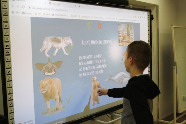 Na zdjęciu ukazany jest uczestnik zajęć edukacyjnych, który zaznacza na tablicy interaktywnej niedźwiedzia. Na tablicy widać również inne zwierzęta: wilka, hienę, wieloryba, panterę.