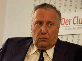 Na zdjęciu ukazany jest pisarz Frederick Forsyth. Widać tylko jego popierskie. Jest ubrany w szary garnitur w delikatne, ledwo widoczne paski, białą koszulę oraz granatowy krawat z żółtymi elementami ozdobnymi.