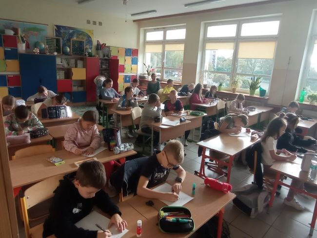 Uczniowie siedzą przy stolikach i wykonują prace plastyczne.
