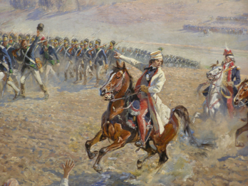 Ilustracja przedstawia fragment obrazu "Panorama Racławicka" eksponowanego w Muzeum Narodowym we Wrocławiu. Na fragmencie jest widoczny Tadeusz Kościuszko na koniu, który zagrzewa do walki swój odział, wskazując prawą ręką kierunek natarcia.