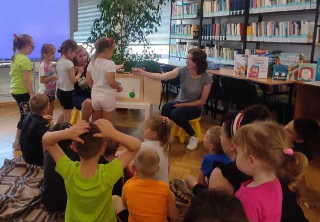 Nauczyciel bibliotekarz częstuje dzieci zielonym groszkiem