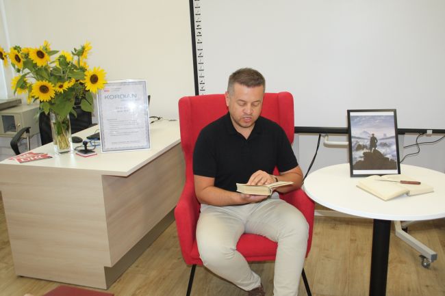 Nauczyciel Biblioteki Pedagogicznej w Zamościu czyta fragmenty Kordiana Juliusza Słowackiego. Na stoliku, przy którym osoby czytają, znajduje się w przezroczystej ramce wydrukowany obraz 