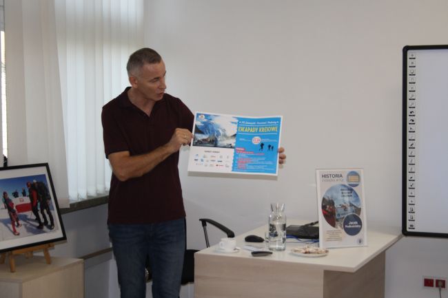 Jacek Podkościelny prezentuje plakat 10-tego Zamojskiego Festiwalu Podróży Eskapady Kresowe.