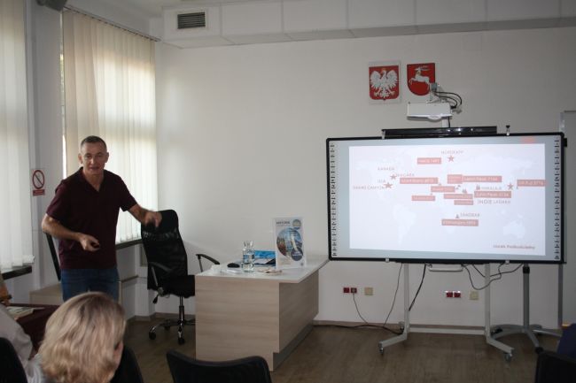 Jacek Podkościelny opowiada przy tablicy multimedialnej o swoich podróżach. Na tablicy jest mapa, na której podróżnik zaznaczył miejsca, do których podróżował w ostatniej dekadzie.