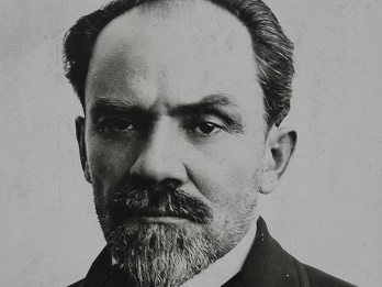 Czarno-białe zdjęcie Stefana Żeromskiego z około 1915 roku. Zdjęcie przedstawia popiersie pisarza, który jest ubrany w płaszcz. Żeromski na zdjęciu posiada krótką brodę i wąsy oraz duże brwi. Włosy ma zaczesane do tyłu, nieco przerzedzone na środku głowy. Patrzy prosto w obiektyw.