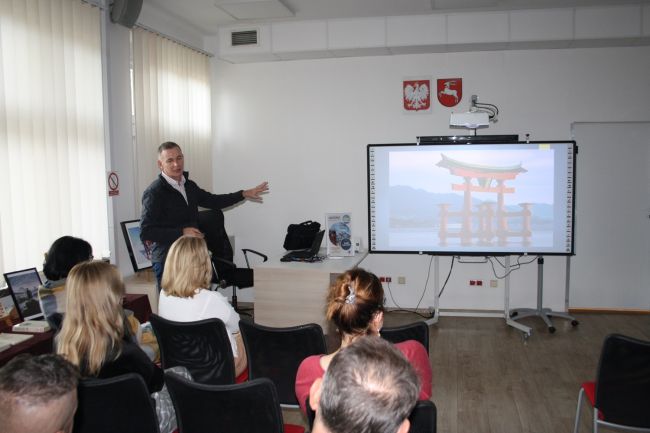 Jacek Podkościelny wskazuje ręką na slajd wyświetlający się na tablicy multimedialnej, który prezentuje ciekawą konstrukcję w Japonii.