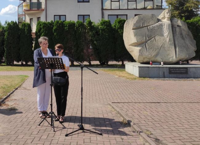 Kobiety stojące przy mikrofonie, w tle pomnik