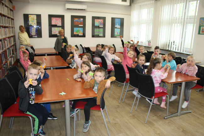Zdjęcie przedstawia grupę przedszkolaków, którzy uczestniczyli w zajęciach w czytelni Biblioteki Pedagogicznej w Zamościu. Dzieci prezentują wykonane przez siebie prace plastyczne.