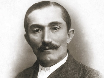 Zdjęcie Wincentego Witosa z 1920 roku. Witos ubrany jest w marynarkę, kamizelkę i koszulę. Ma wąsy, trochę odstające włosy, fryzura krótka z przedziałkiem po lewej stronie.