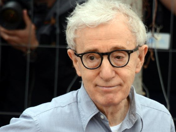 Zdjęcie wykonane w Cannes w 2016 roku. Woody Allen jest w charakterystycznych dla siebie okrągłych okularach. Ubrany jest w jednolitą koszulę z długim rękawem. Lekko się uśmiecha.