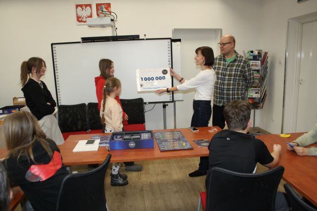 Prowadząca zajęcia wręcza zwycięskiej drużynie symboliczny czek na kwotę miliona złotych z logo Biblioteki Pedagogicznej.
