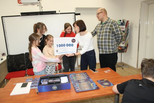 Prowadząca zajęcia wręcza zwycięskiej drużynie symboliczny czek na kwotę miliona złotych z logo Biblioteki Pedagogicznej.
