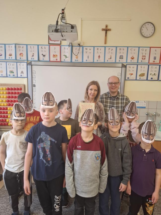 Uczniowie prezentują wykonane przez siebie podczas zajęć maski Niesfornego Ziarenka. Nauczyciele stoją za uczniami.