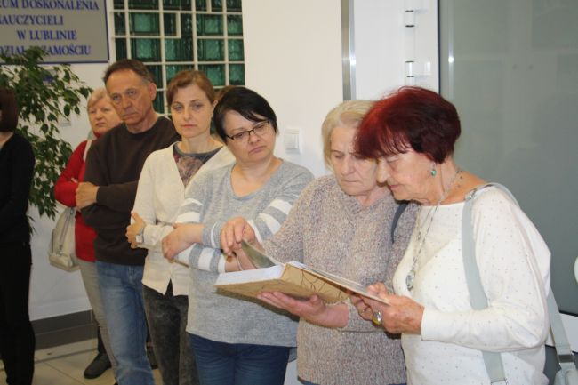 Uczestniczki finisażu oglądają album z pracami Reginy Grzybowskiej.
